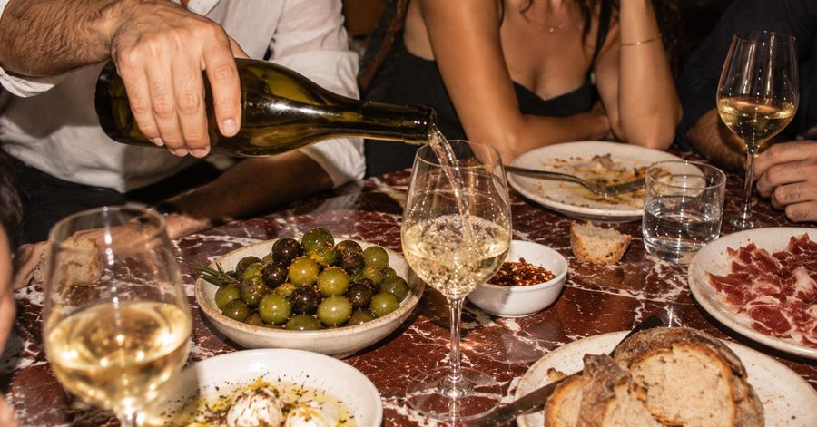 White wine poured over a bowl of olives on a red marble table