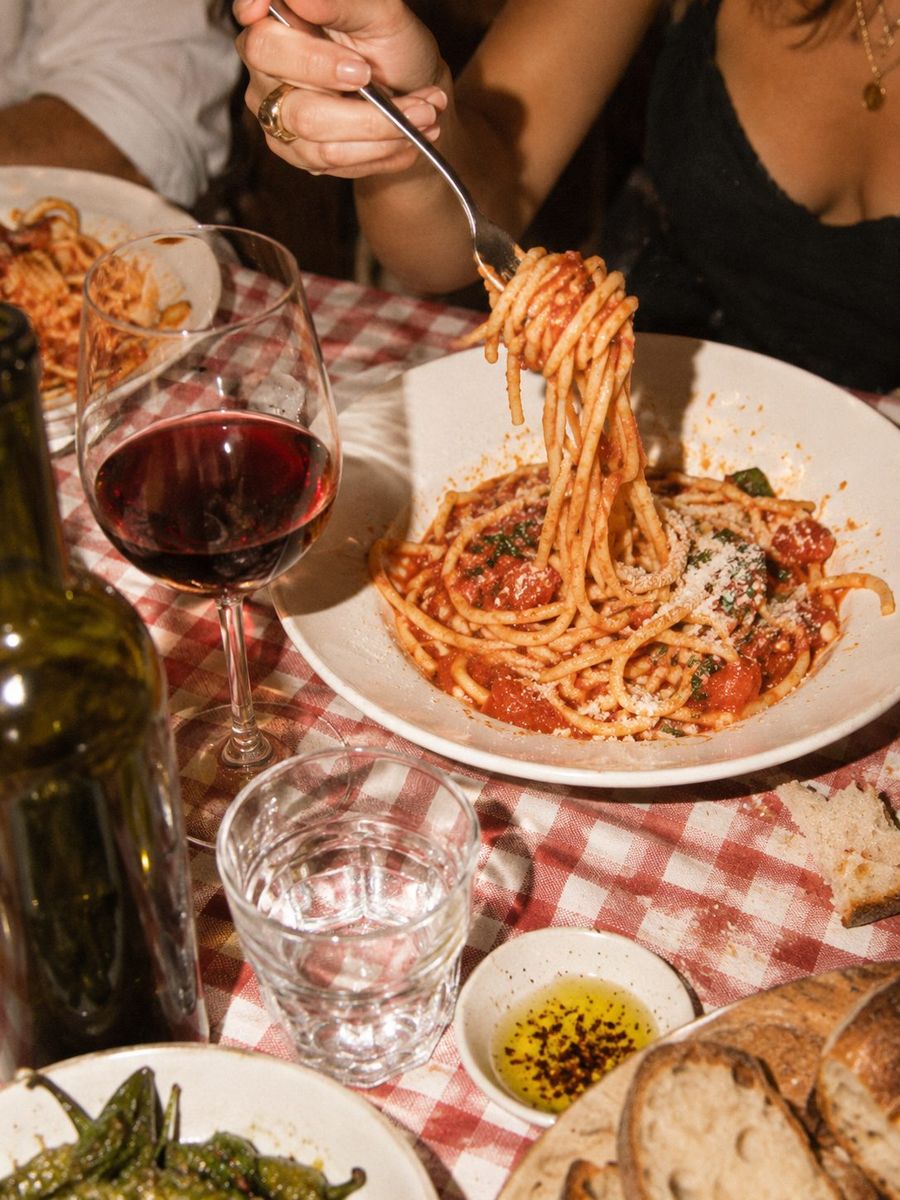 Spaghetti twirled on a fork next to a glass of red wine